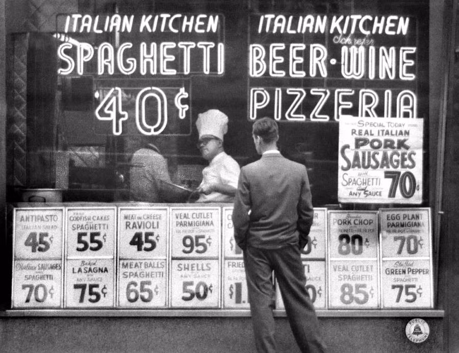 Một người đàn đứng trước cửa hàng đồ ăn Italy năm 1956.