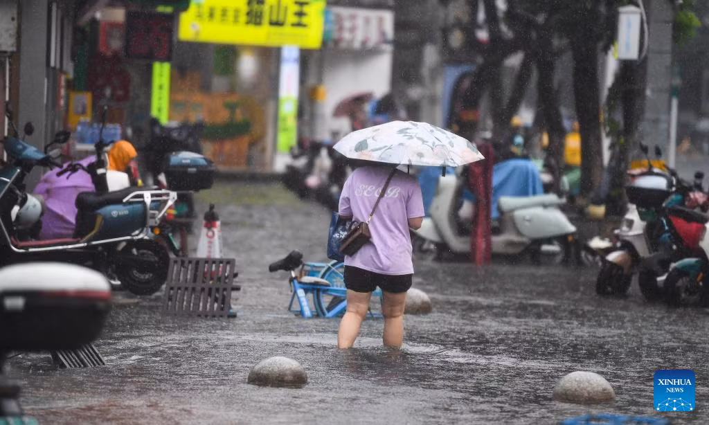 Người phụ nữ che ô lội qua khu vực ngập lụt ở Hải Khẩu, tỉnh Hải Nam.