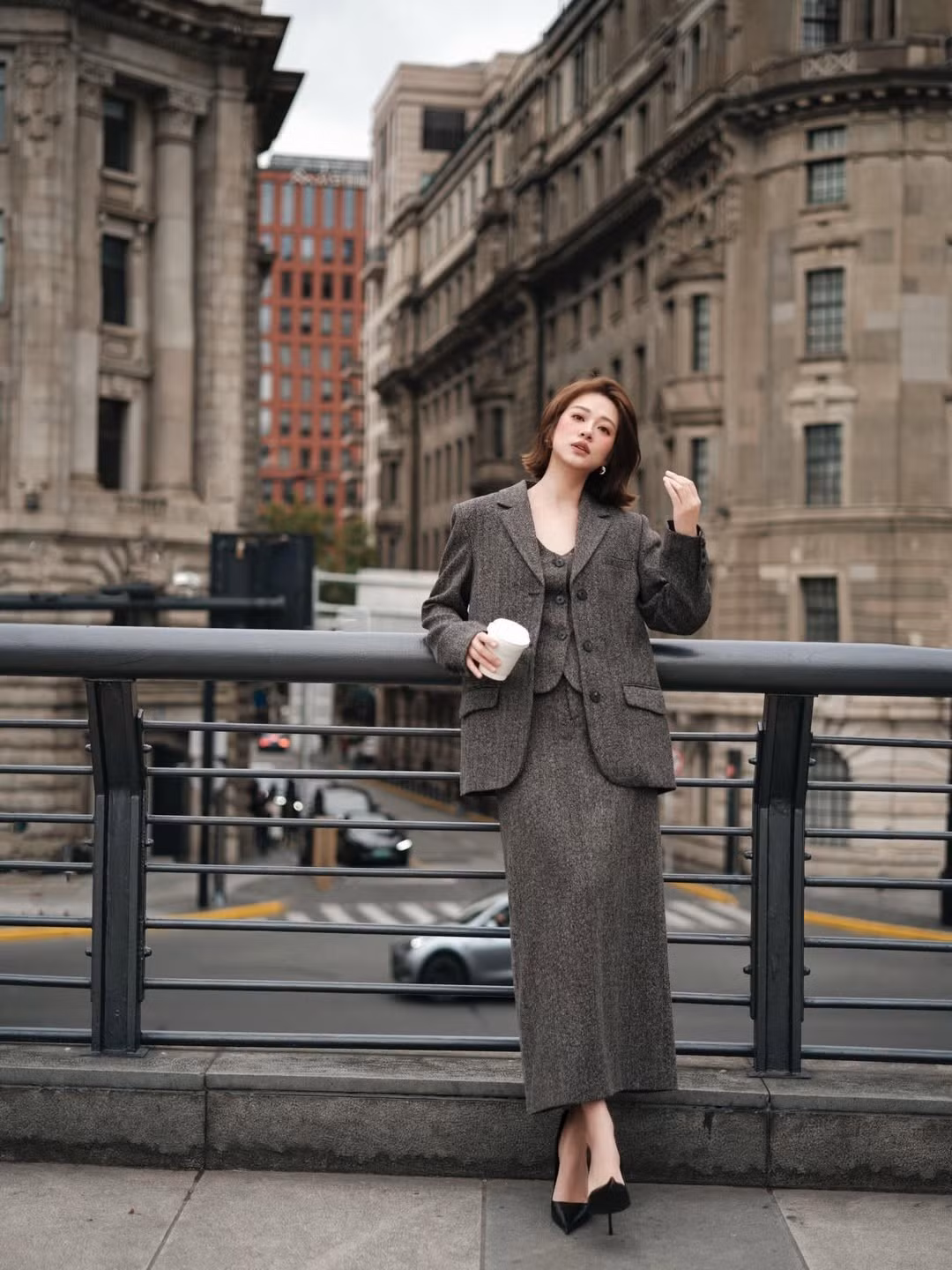 Ở mỗi shoot hình, gương mặt của Mai Anh toát lên vẻ nhẹ nhàng nhưng không kém phần sắc sảo. Làn da sáng mịn, makeup tông nâu – hồng tự nhiên giúp tôn lên các đường nét hài hòa. Mái tóc ngắn uốn cụp tạo cảm giác cổ điển, rất hợp với bối cảnh những tòa nhà đá xám đậm chất Thượng Hải cổ.