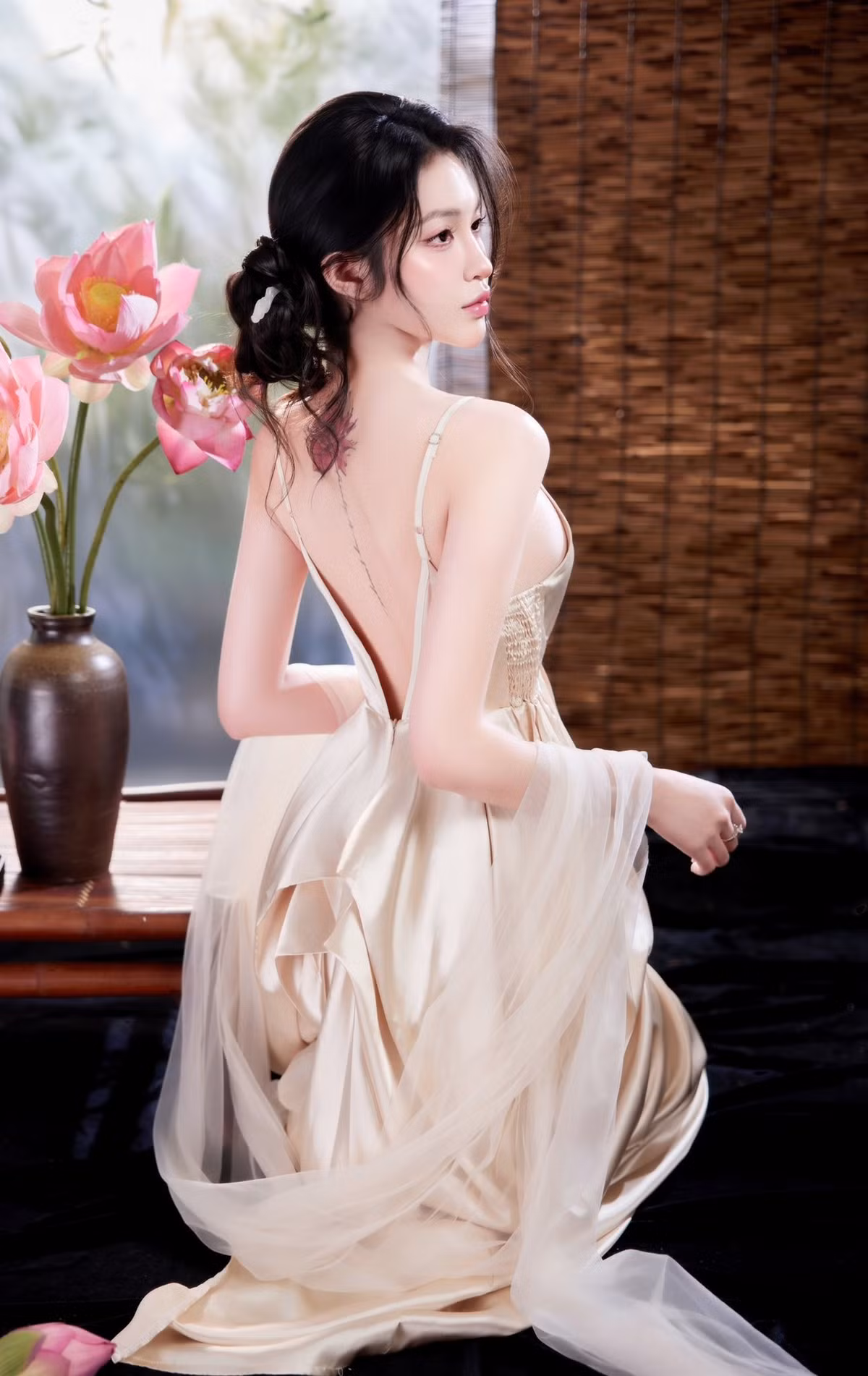Chiếc đầm lụa màu nude/vàng champagne khoét sâu, thiết kế lưng trần táo bạo đã tạo nên sự tương phản thú vị. Nếu hoa sen tượng trưng cho sự thanh cao, thì chiếc đầm lại tôn lên trọn vẹn đường cong và vẻ quyến rũ hiện đại của Triều Tiên.