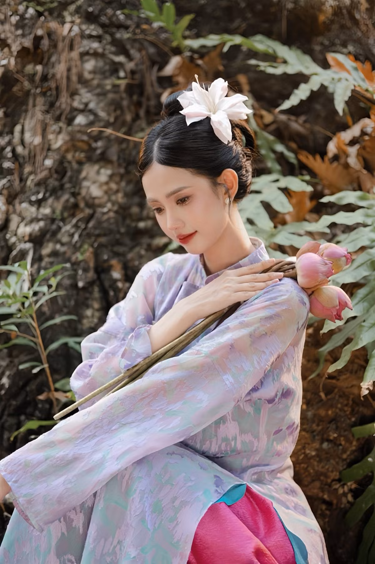 Trong bộ ảnh, Gabriella Bùi diện thiết kế áo dài mang tông tím pastel pha sắc hồng nhẹ, tạo cảm giác mềm mại và lãng mạn. Chất liệu vải mỏng, bay nhẹ theo từng chuyển động giúp tà áo thêm phần thướt tha, uyển chuyển giữa khung cảnh thiên nhiên rợp bóng cây xanh.