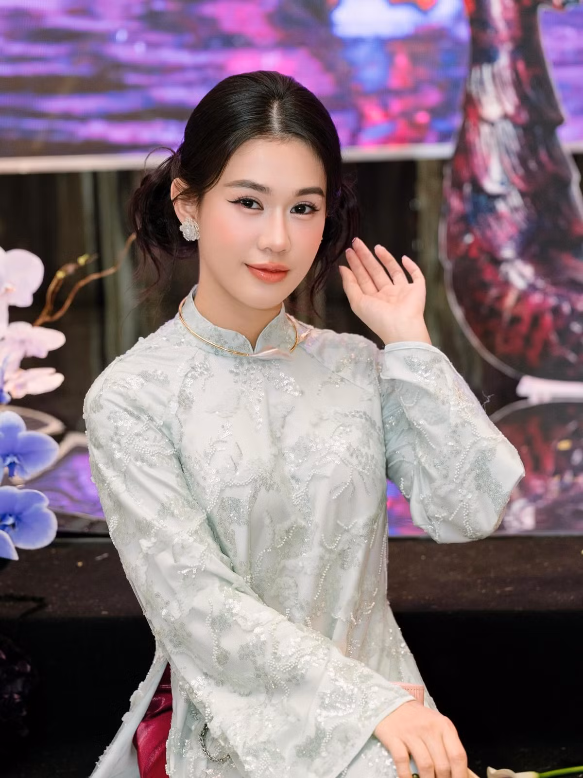 Trong loạt ảnh được chia sẻ, Ngọc Thảo diện áo dài tông xanh pastel nhẹ nhàng, chất liệu thêu ánh kim tinh tế, tạo hiệu ứng mềm mại và sang trọng. Thiết kế cổ cao, tay dài cùng phom dáng suông truyền thống giúp tôn lên vóc dáng thanh thoát dù cô chỉ cao 1m62. Khi kết hợp cùng quần lụa hồng trầm và phụ kiện quạt tay, tổng thể trang phục mang đến cảm giác nền nã, hoài cổ nhưng không kém phần cuốn hút.