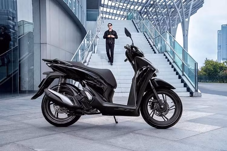 Về thiết kế, SH160i/125i 2027 không thay đổi. Phiên bản Thể thao có bổ sung phối màu đen "Aura Black Edition" mới với tông màu đen bao phủ thân xe, ngàm phanh, lò xo giảm xóc và tay dắt sau, điểm xuyết chi tiết chữ V mặt nạ trước cùng logo SH mạ chrome.