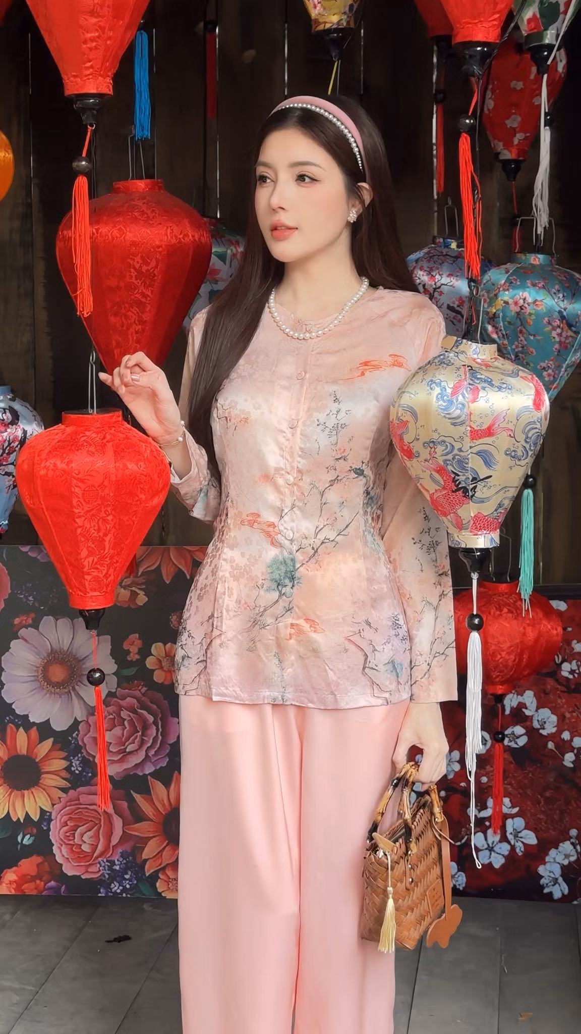 Thiết kế áo bà ba được biến tấu nhẹ với chất liệu vải bóng mịn, in họa tiết hoa lá và chim chóc mang hơi hướng tranh thủy mặc. Phom dáng vẫn giữ nét đặc trưng cổ tròn, hàng nút giữa thân áo, nhưng được xử lý tinh tế hơn để tôn lên vóc dáng mảnh mai của Lilly Luta.