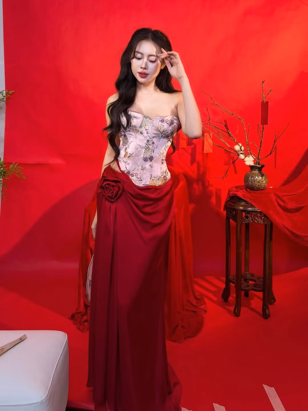 Trong bộ ảnh đón xuân, Việt Phương Thoa lựa chọn phong cách gợi cảm pha nét truyền thống. Thiết kế corset thêu hoa kết hợp chân váy đỏ rực giúp tôn lên đường cong cơ thể, đồng thời hòa cùng sắc đỏ đặc trưng của ngày Tết. Phông nền đơn sắc cùng các đạo cụ như cành lộc, phong bao lì xì tạo nên bầu không khí xuân rộn ràng nhưng vẫn giữ được tinh thần thời trang hiện đại.