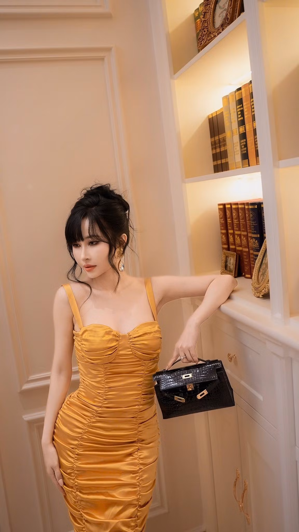 Trong những khung hình được chia sẻ, Mina Phạm lựa chọn thiết kế đầm hai dây gam vàng ánh kim, phần thân được xếp ly dọc tinh tế giúp tôn lên đường cong mềm mại.