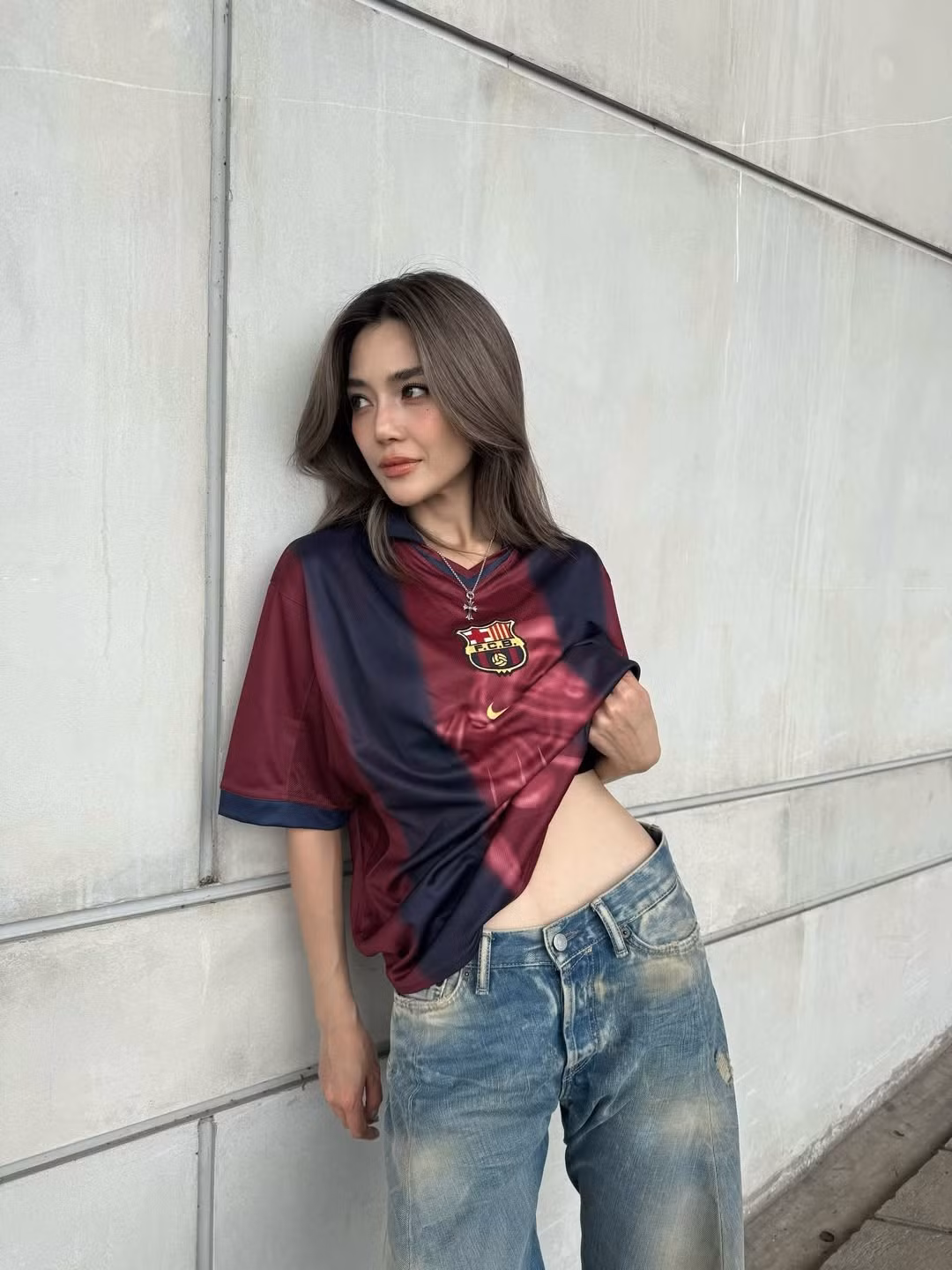 Trong những khung hình được chia sẻ, Prang Kannarun lựa chọn áo đấu Barca form rộng, buộc gọn phần gấu áo để khéo léo khoe vòng hai phẳng lì. Cô phối cùng quần jeans ống suông bụi bặm, sneakers trắng và trang sức tối giản, tạo nên tổng thể street style vừa cá tính vừa gợi cảm.