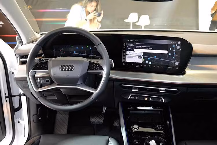 Một trong những thay đổi đáng chú ý nhất là việc Audi loại bỏ cần số truyền thống ở bệ trung tâm và thay thế bằng lẫy điều khiển điện tử tích hợp trên trục vô-lăng. Thiết kế này không chỉ tối ưu thao tác cho người lái mà còn giải phóng đáng kể không gian nội thất, tạo điều kiện bố trí sạc điện thoại không dây 15W có chức năng làm mát, hộc chứa đồ lớn và các tiện ích sử dụng hàng ngày.