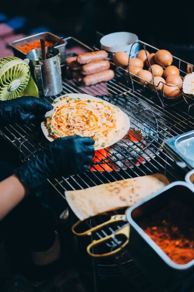 Nhắc đến chợ đêm Đà Lạt, bánh tráng nướng là món ăn đầu tiên được nhiều du khách lựa chọn. Những quầy bánh san sát nhau, luôn đỏ lửa suốt buổi tối. Từ chiếc bánh tráng mỏng, người bán khéo léo kết hợp trứng, mỡ hành, tép khô, xúc xích, phô mai… tạo nên món ăn giòn rụm, béo bùi, đậm đà. Mỗi quầy có cách nêm nếm riêng, mang đến hương vị khác biệt, đủ để thực khách ăn một lần là nhớ mãi. Ảnh Nguyên Phú