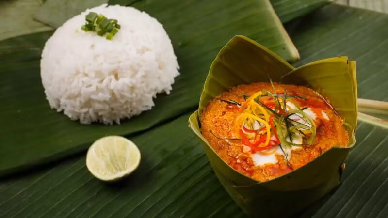 Khi nhắc đến ẩm thực xứ Chùa Tháp, khó có thể bỏ qua fish amok – món ăn được xem như biểu tượng quốc gia. Cá tươi được nấu cùng nước cốt dừa, trứng và hỗn hợp gia vị kroeung gồm sả, riềng và nghệ, sau đó hấp trong lá chuối. Thành phẩm có vị béo nhẹ, thơm nồng nhưng không ngấy, phản ánh sự tinh tế trong cách nêm nếm của người Khmer. Ảnh Traveloka