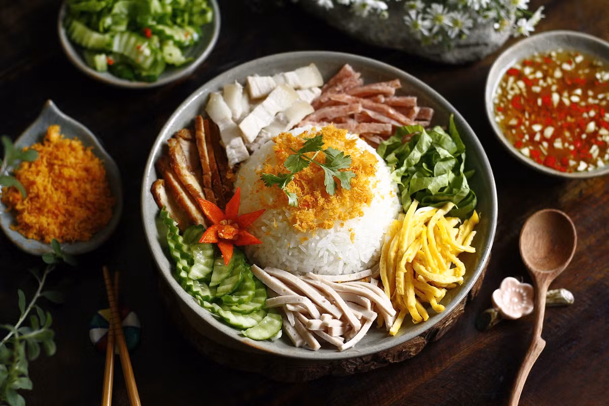 Điều làm nên sức hút của cơm Âm phủ không chỉ nằm ở phần nhìn mà còn ở sự cân bằng trong hương vị. Vị mặn ngọt của thịt rim, độ dai của chả, chút béo từ trứng, chút chua của đồ chua và độ tươi của rau sống hòa quyện cùng nhau, tất cả gói trọn trong từng muỗng cơm nóng hổi.