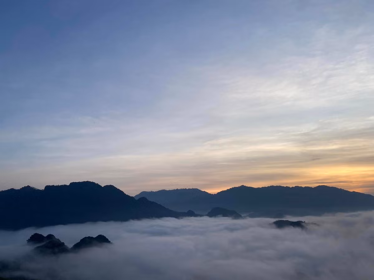 Khoảnh khắc đáng giá nhất là khi mặt trời vừa ló rạng. Mây cuộn dưới thung lũng, bản làng và ruộng nương thấp thoáng phía xa. Khi nắng lên, biển mây dần tan, để lộ bức tranh trung du với những gam màu dịu nhẹ của núi đồi và nếp nhà sàn. Ảnh Fanpage Đèo Cón Chill