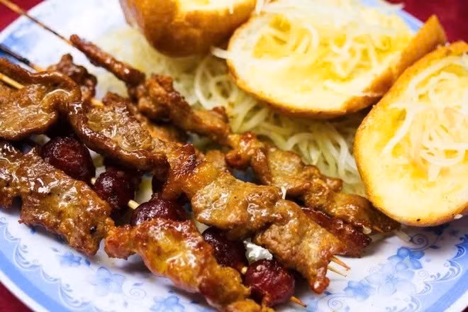 Cũng từ những bếp than ven đường, sach ko ang jakok – bò xiên sả nướng – tỏa mùi thơm quyến rũ. Thịt bò được ướp kroeung, nướng xém lửa, ăn kèm bánh mì baguette nướng bơ và salad chua, thể hiện rõ nét sự giao thoa giữa ẩm thực Khmer và ảnh hưởng Pháp. Ảnh Internet