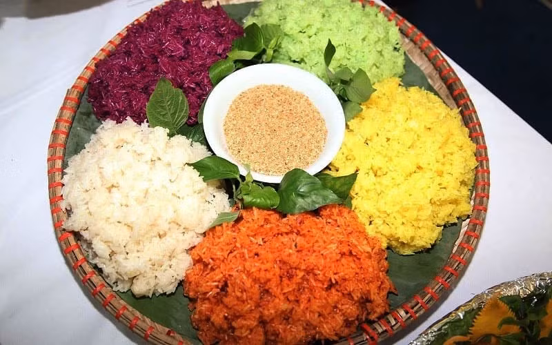 Nếu muốn tìm chút sắc màu rực rỡ, xôi ngũ sắc là món ăn không thể bỏ qua. Nếp được nhuộm từ các loại lá rừng, nghệ, lá cẩm tạo nên năm màu tượng trưng cho ngũ hành. Xôi ăn cùng lạc giã dập hoặc rưới chút nước cốt dừa béo ngậy, vừa đẹp mắt vừa đậm đà bản sắc. Ảnh dulichviet