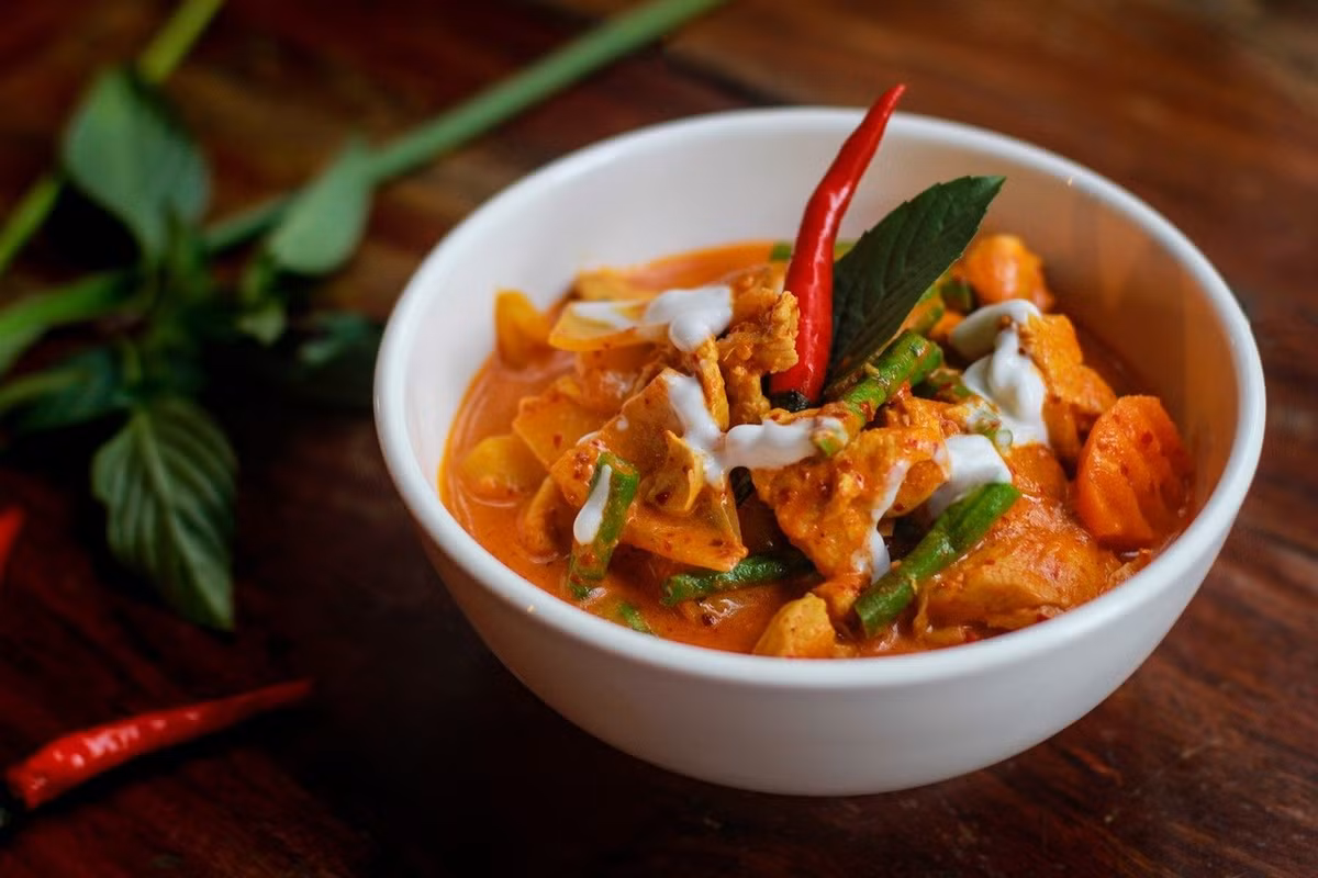 Ẩm thực Campuchia không chỉ có những món ăn nhanh, mà còn mang đến cảm giác ấm áp qua những món “comfort food” quen thuộc. Na tang là một ví dụ tiêu biểu, với thịt heo băm chiên vàng đặt trên nền cà ri dừa – đậu phộng đỏ sánh mịn, ăn kèm bánh gạo phồng chiên giòn. Món ăn béo, bùi, thường xuất hiện trong những bữa cơm gia đình. Ảnh iVIVU
