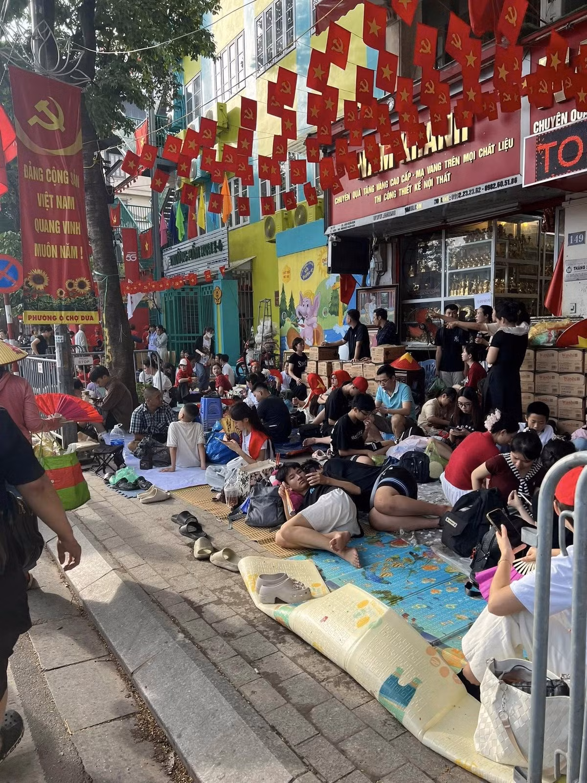 Từng nhóm gia đình, bạn trẻ, người lớn tuổi trải bạt, chiếu để chờ xem diễu binh, diễu hành 2/9.