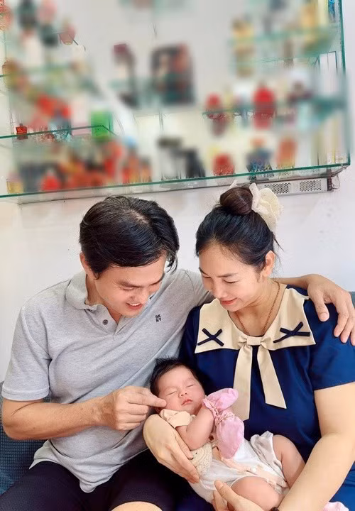 Hình ảnh vợ chồng Cao Minh Đạt cùng cúi xuống ngắm con ngủ, ánh nhìn trìu mến dành cho con, tạo nên một bức tranh gia đình giản dị mà ấm áp.