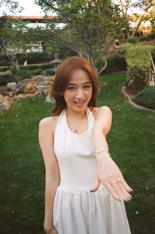 Xuân Nghi đăng tải hình ảnh diện váy trắng giữa khu vườn xanh mướt, nở nụ cười rạng rỡ khi đưa tay khoe nhẫn đính hôn. Khoảnh khắc không quá phô trương, nhưng đủ để thấy niềm hạnh phúc hiện rõ trên gương mặt cô.