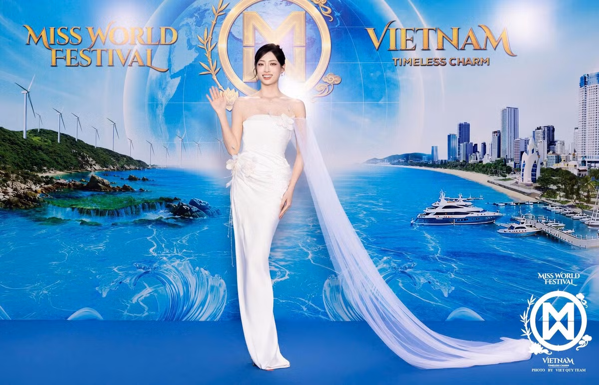 Hoa hậu Lương Thùy Linh diện váy trắng ôm dáng, điểm xuyết chi tiết hoa nổi ở phần thân. Dải voan dài từ vai kéo xuống sàn tạo điểm nhấn. Người đẹp búi tóc cao, kết hợp vòng cổ và hoa tai nhỏ.