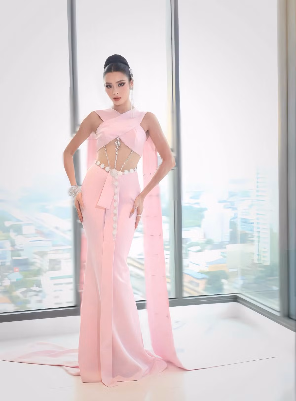 Emoura Phạm thử nghiệm thiết kế màu hồng với những khoảng cut-out ở eo, kết hợp chi tiết đính kết chạy dọc thân. Kiểu tóc búi cao và cách tạo dáng nhấn vào lợi thế hình thể của người đẹp.