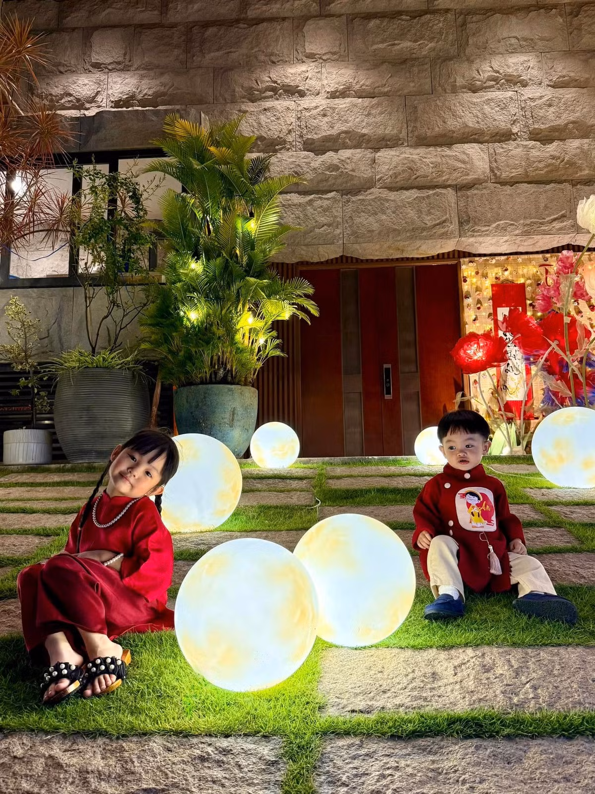 Bé Suchin diện áo dài đỏ truyền thống, phom dáng rộng rãi, kết hợp các phụ kiện nhỏ xinh như vòng cổ, dép đính hạt. Ảnh: Instagram Suchin - Sutin.