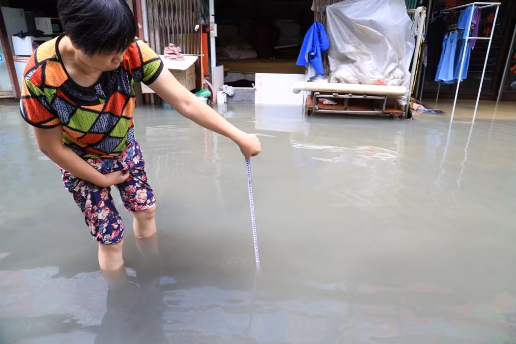 Người phụ nữ mang thước dây ra đo mực nước mưa ở ngoài đường.