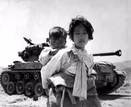 Một bé gái cõng em đi qua chiếc xe tăng M-26 bị chết máy, tháng 6/1951.