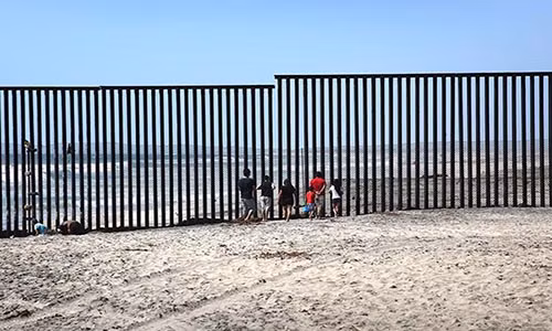 Những người dân Mexico đứng trên bãi biển ở Tijuana ngày 1/5/2016 nhìn sang nước Mỹ qua bức tường thép ngăn cách Mỹ-Mexico.