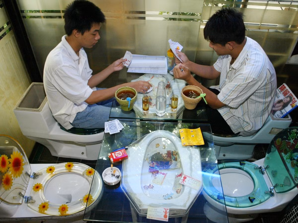 Khách hàng ngồi chơi bài trên ghế bồn cầu tại một nhà hàng theo chủ đề nhà vệ sinh ở Thâm Quyến, tỉnh Quảng Đông, Trung Quốc. Thực khách sử dụng bồn cầu để ngồi như ghế khi họ ăn thức ăn phục vụ trong các bồn cầu nhỏ.