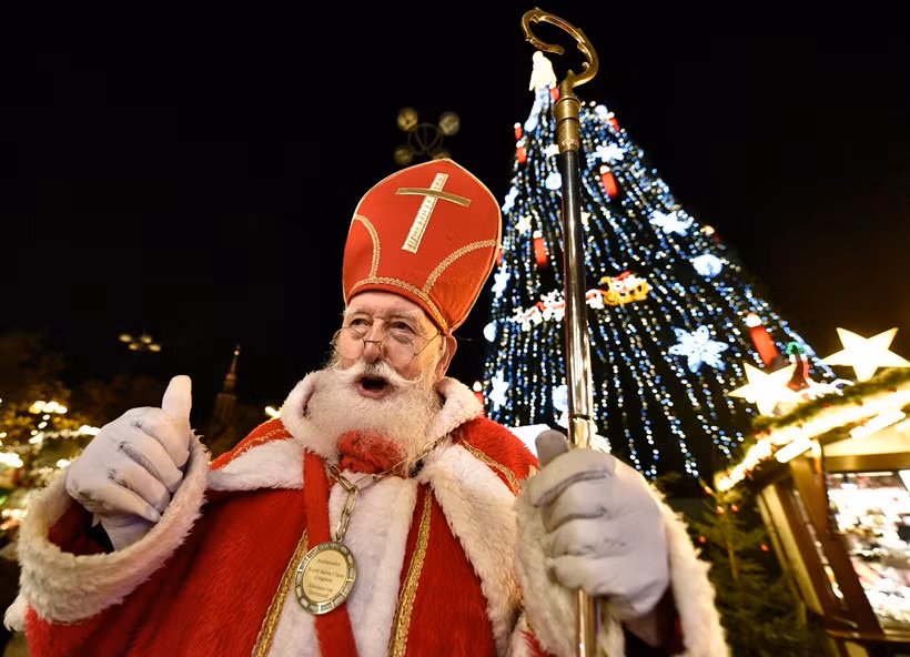 Một người đàn ông hóa trang thành ông già Noel Santa Claus đứng trước cây thông Giáng sinh lớn nhất của Đức, được chiếu sáng bởi 48.000 bóng đèn chiếu sáng tại chợ Giáng sinh ở Dortmund, Đức. Cây thông cao 45m này được xây dựng từ 1.700 cây vân sam.