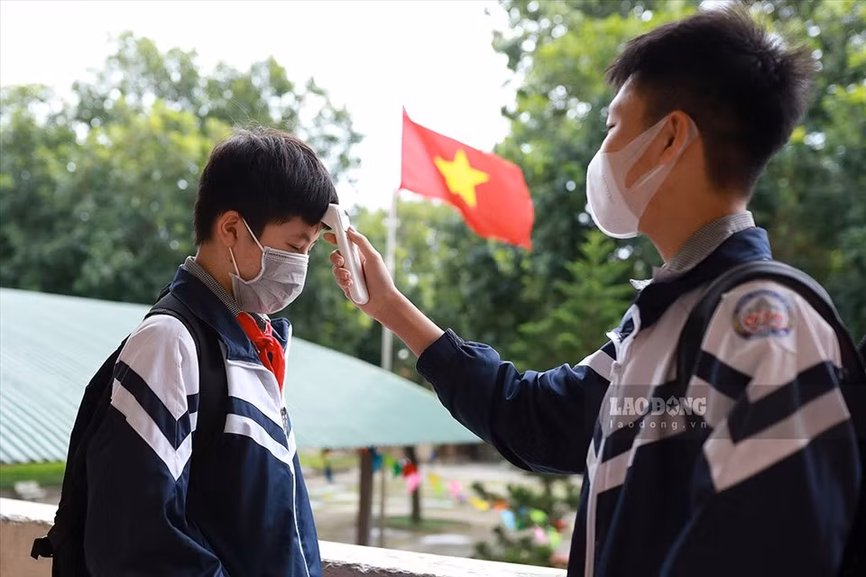 Các em kiểm tra thân nhiệt, sát khuẩn tay rồi được dẫn về lớp theo các luồng di chuyển định sẵn, thay vì tự do đi lại như trước. Em Đỗ Đức Mạnh - học sinh lớp 9E đo thân nhiệt cho các bạn trước và sau khi tan học. (Ảnh: Lao Động)