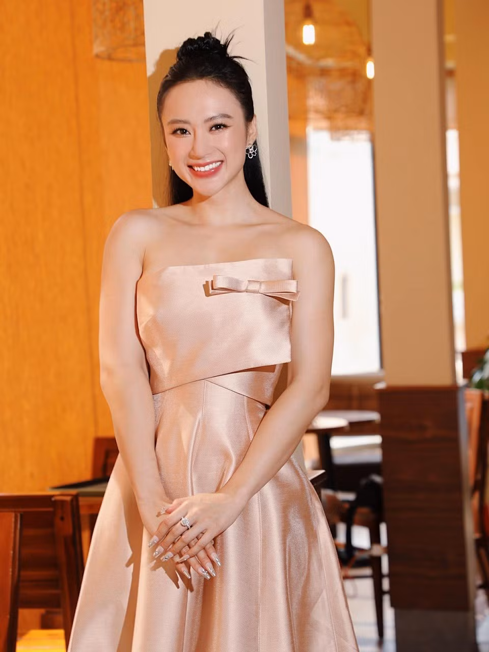 Angela Phương Trinh mặc bộ váy hồng pastel nhẹ nhàng, kết hợp trang sức điệu đà, để lộ vai và tay trong một buổi đi phỏng vấn.