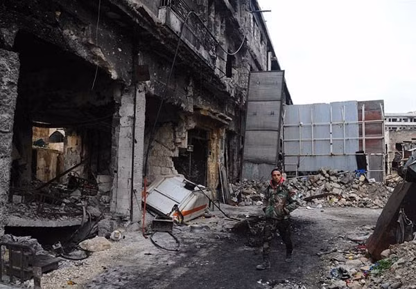 Một binh sĩ Syria đứng trước tòa nhà đổ nát ở Aleppo. 