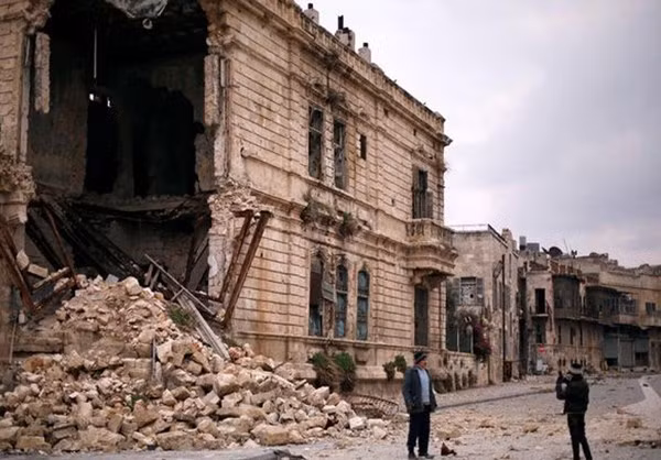 Người đàn ông tạo dáng khi đứng trước một tòa nhà đổ nát ở thành phố Aleppo.