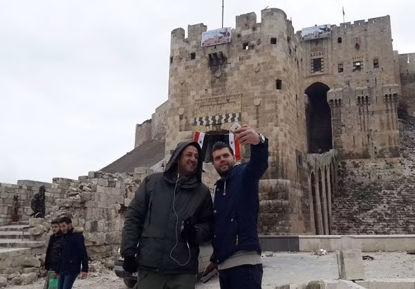 Hai người đàn ông dùng điện thoại chụp ảnh khi đứng trước Thành cổ Aleppo.