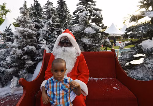 Một cậu bé ngồi với ông già Noel ở khu vườn trong cung điện tổng thống ở Abidjan trong lễ Giáng sinh vừa qua.