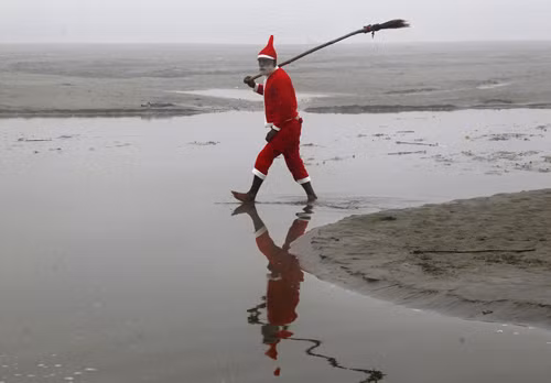 Một người theo đạo Hindu mặc đồ ông già Noel thu dọn rác thải ở bờ sông Ganges, thành phố Allahabad, Ấn Độ.