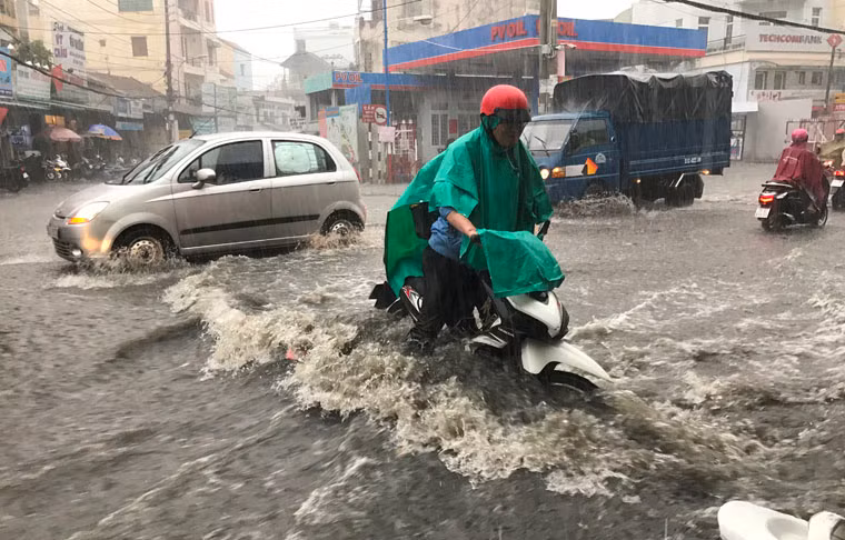 Xe cộ bì bõm lội qua vùng ngập nước trong cơn mưa đầu mùa giữa trưa ở TP HCM.