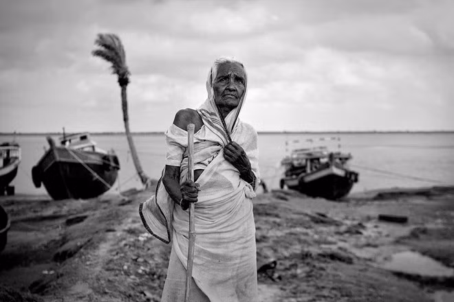 Bà Chaya Mondal, 76 tuổi, đứng chờ ở bờ biển để đón người thân trở về sau một ngày đánh bắt cá. Bà đã sống gần cả đời trên đảo Ghoramara và không muốn chuyển đến nơi ở mới dù biết rằng nó đang chìm dần.