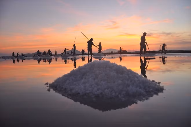 Bầu trời hừng lên trên cánh đồng muối Hòn Khói (Ninh Hòa). Trông từ xa, cánh đồng như một tấm gương lớn phản chiếu ánh bình mình và cả dáng những diêm dân một nắng hai sương.