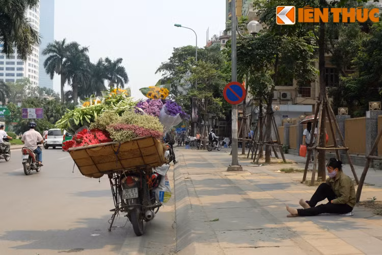Người phụ nữ bán hoa dạo ngồi nghỉ chân dưới một tán cây xanh để tránh nắng.
