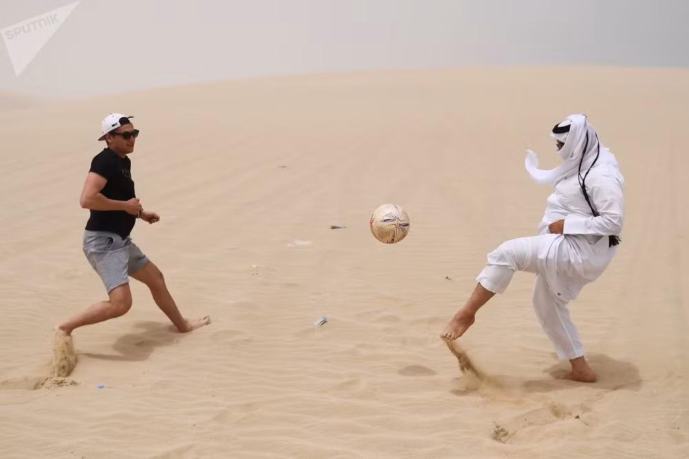 Hai người đàn ông chơi đá bóng trên sa mạc Khor Al Adaid, thủ đô Doha, Qatar.