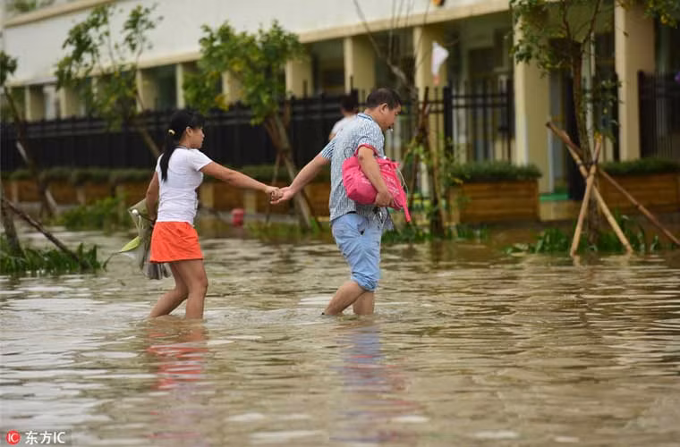 Đôi nam nữ dắt tay nhau qua đoạn đường ngập nước do bão Sarika gây nên ở thành phố Quỳnh Hải sáng 18/10.