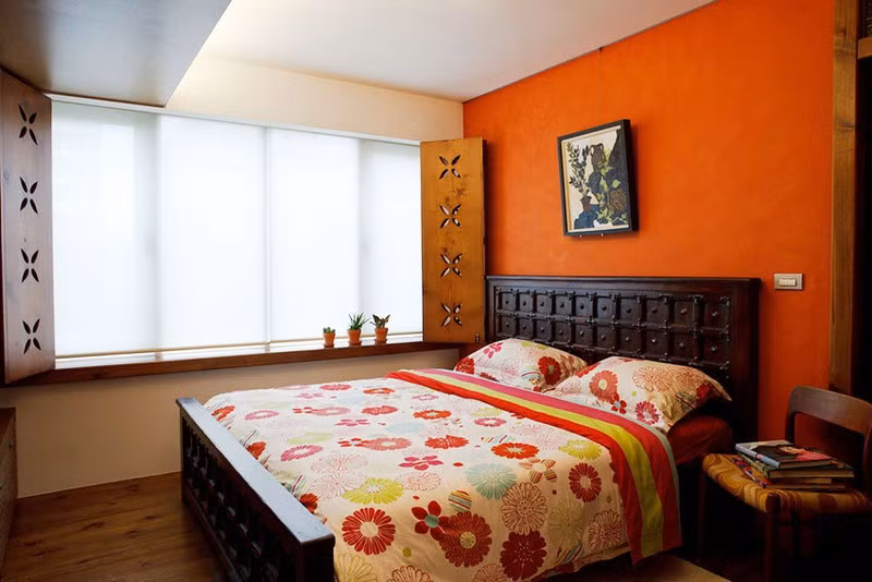Chiếc giường gỗ chạm khắc tỉ mỉ cùng bức tường đầu giường sơn cam giúp người sử dụng luôn cảm thấy ấm áp và dễ chịu, dễ dàng có được giấc ngủ sâu, thoải mái.