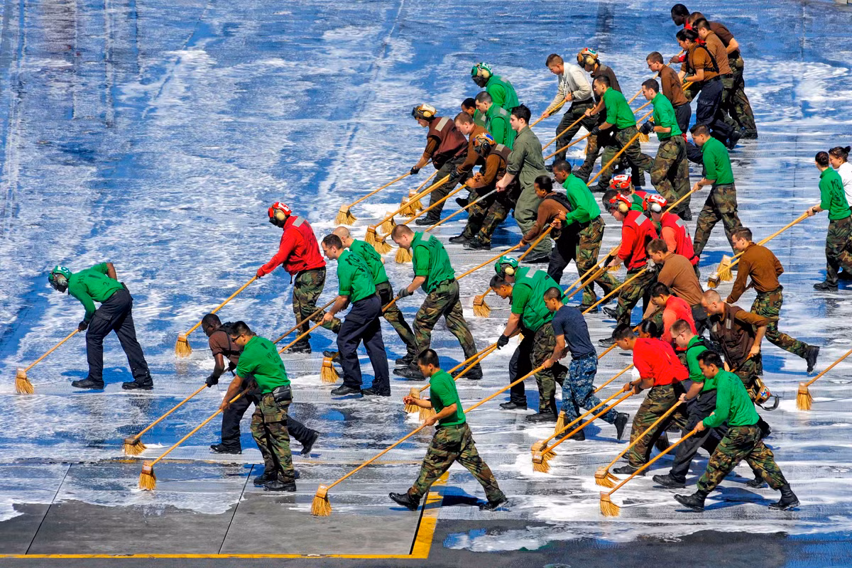 Ngoại trừ những nhân viên VIP mặc áo màu trắng, còn lại toàn bộ các nhân viên khác phục vụ trên sàn tàu sân bay đều phải thực hiện chung một nhiệm vụ đó là... cọ sàn tàu. Nguồn ảnh: Pinterest.