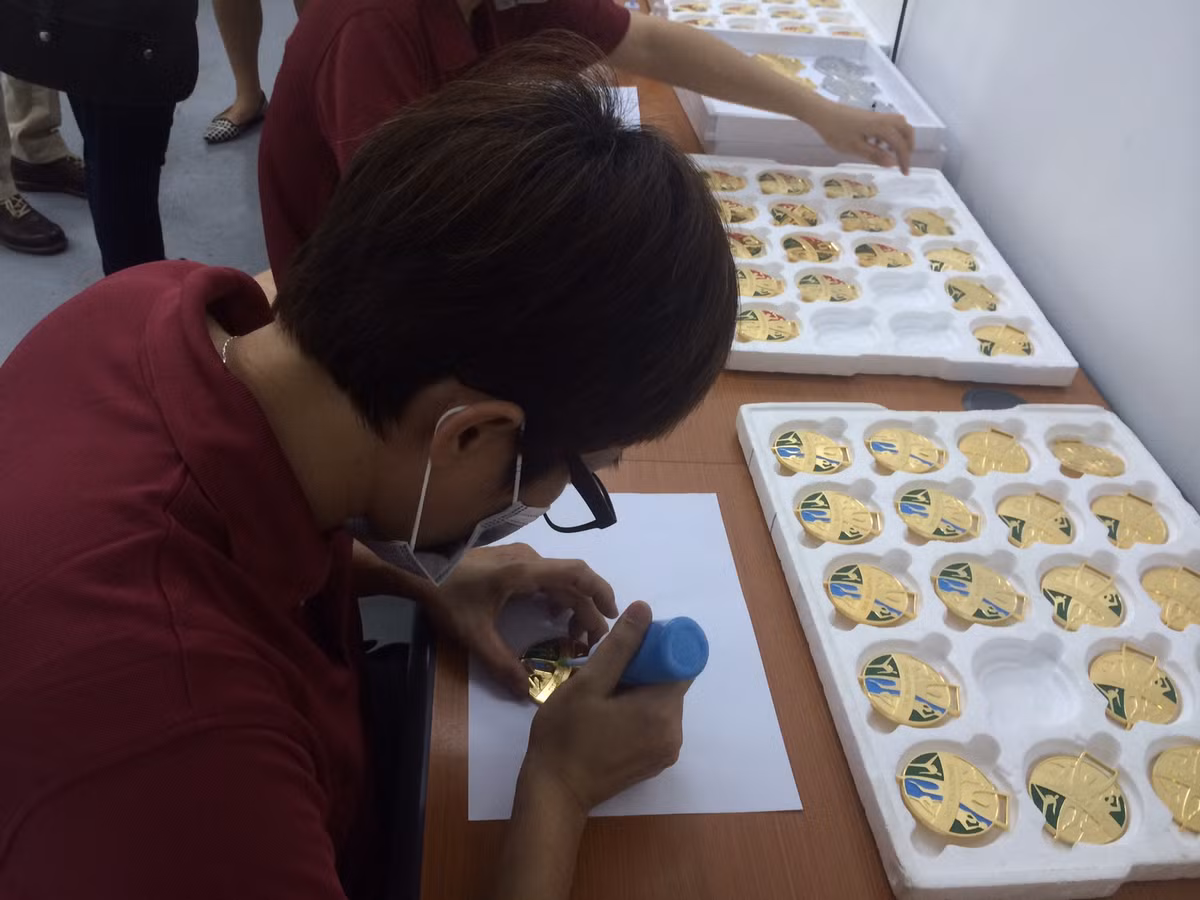 Cuối cùng, các huy chương sẽ được gắn dây ruy-băng và vượt qua khâu kiểm tra chất lượng. Sau khi hoàn tất quá trình này, các huy chương đã sẵn sàng để trao cho các vận động viên xứng đáng.