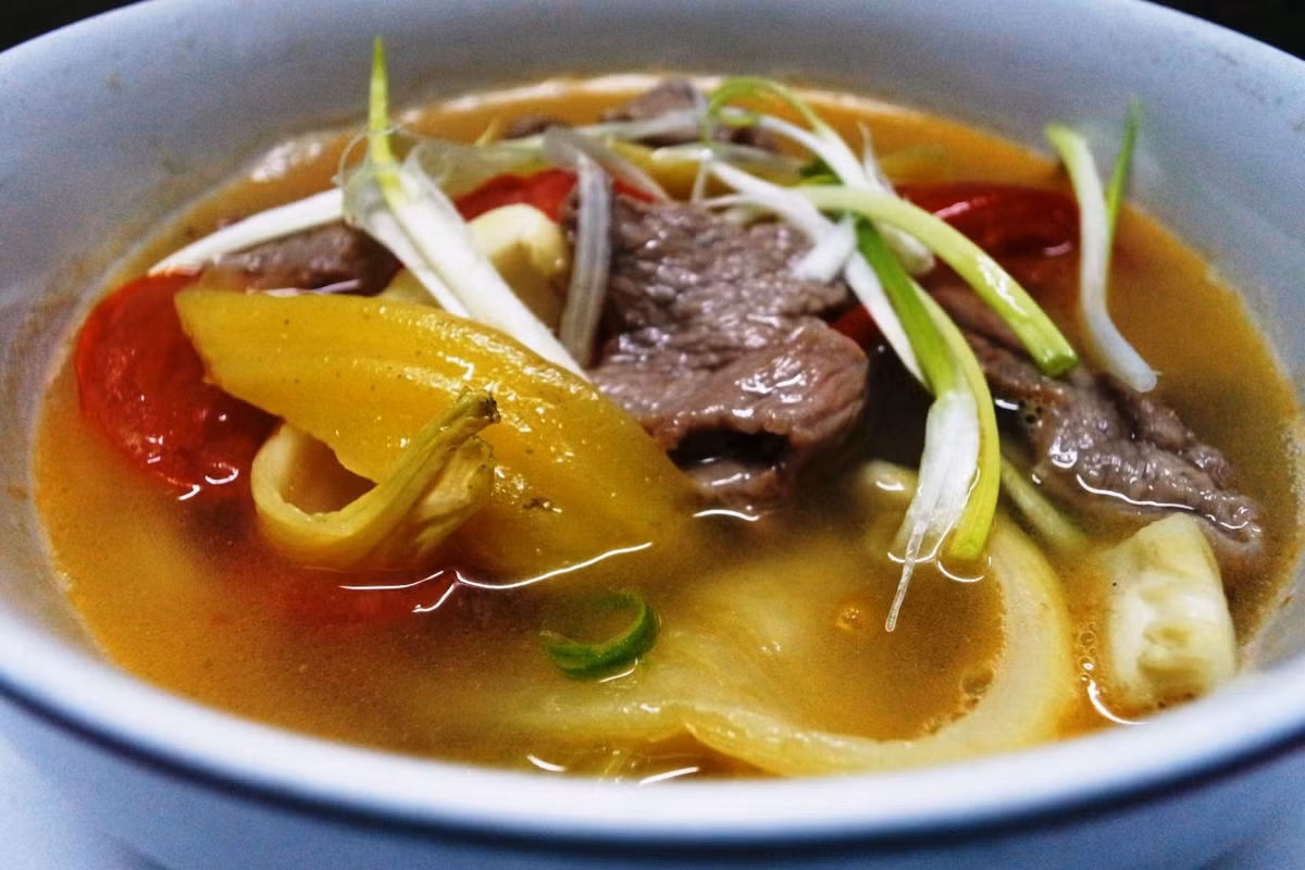 Cho thịt bò vào nồi đun tiếp, cho thêm một chút bột nêm cho thêm đậm đà. Sau đó đổ tất cả vào bát. Cho thêm ớt và hành vào để món ăn thêm đậm đà hương vị. Ảnh: BepGiaDinh.com.