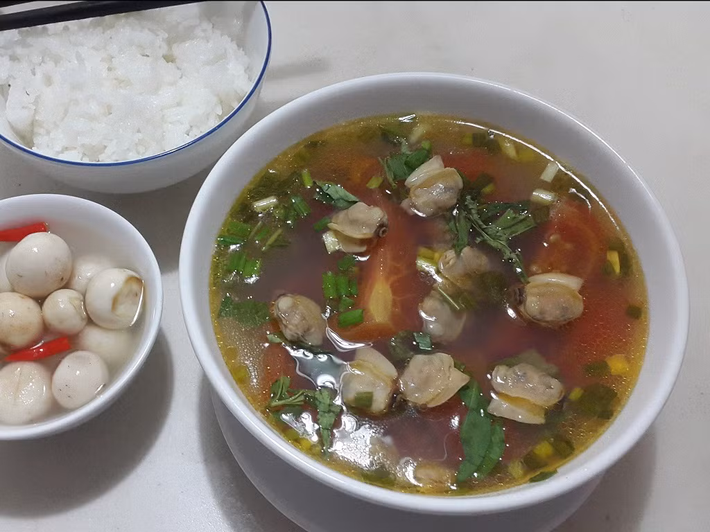 Bắt nồi lên bếp, cho ít dầu ăn vào đợi dầu nóng bỏ hành vào phi thơm lên cho ngao vào đảo qua lại cho thơm. Tiếp tục cho cà chua vào đảo qua rồi cho hết nước luộc ngao vào nấu cho sôi lên. Bỏ hết sấu vào đợi nước sôi lên lại rồi nêm nếm cho vừa ăn và bỏ hành lá và thì là vào rồi tắt bếp. Ảnh: Lamthenao.com.