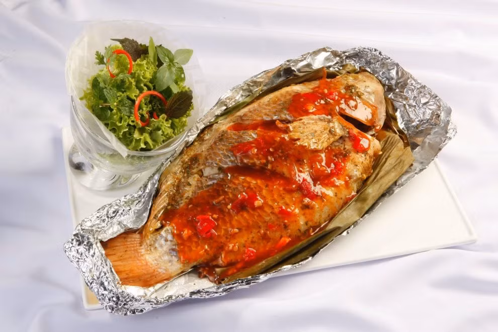 Ướp sốt trên với cá trong 1giờ, xoa đều cho cá ngấm gia vị, bọc màng thực phẩm, để tủ mát. Cá bọc kín giấy bạc, đem nướng lò 25 phút ở 200 độ C. Hành lá, ớt sừng thái chỉ, chanh thái lát mỏng, thì là đã rửa sạch. Rắc lên trên cá sau khi nướng. Ảnh: nhipsongso.edu.vn.