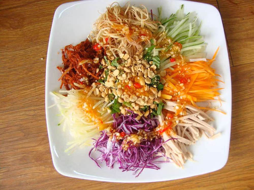 2. Nộm ngũ sắc rau củ. Nguyên liệu: Củ cải đỏ, cà rốt, bắp cải trắng, bắp cải tím, ớt ngọt, khế chua, thịt bò khô, chanh, gia vị, tỏi, ớt, lạc rang, rau thơm. Gọt vỏ, rửa sạch và nạo nhỏ, thái sợi các loại rau củ, rau thơm thái nhỏ. Ảnh: baomoi.com.